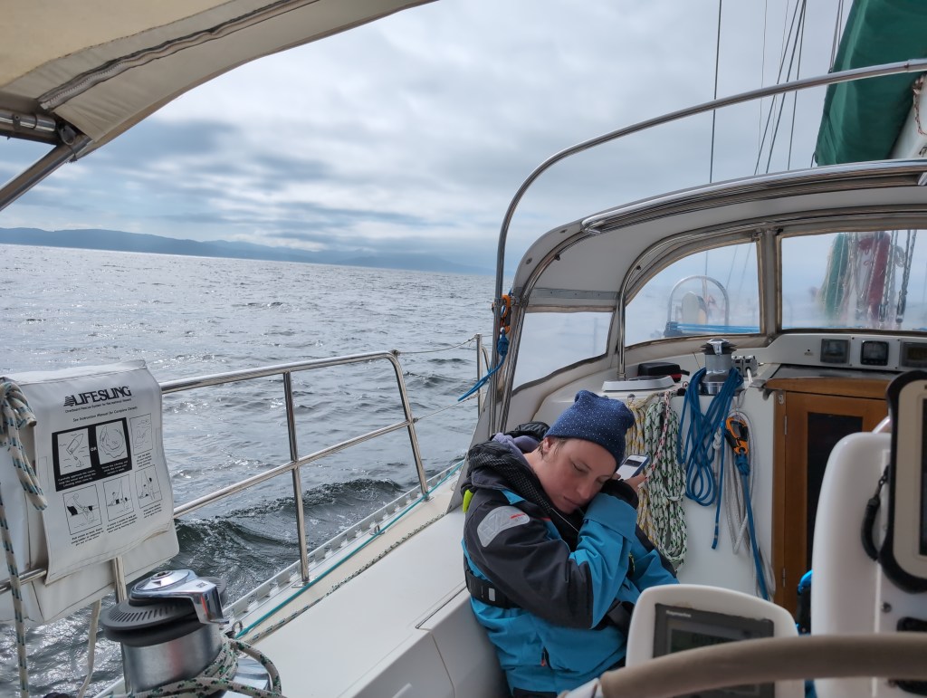 Tiffany tilts her head as she listens to her phone, a hilly shore line visible in the distance beneath low hanging clouds..