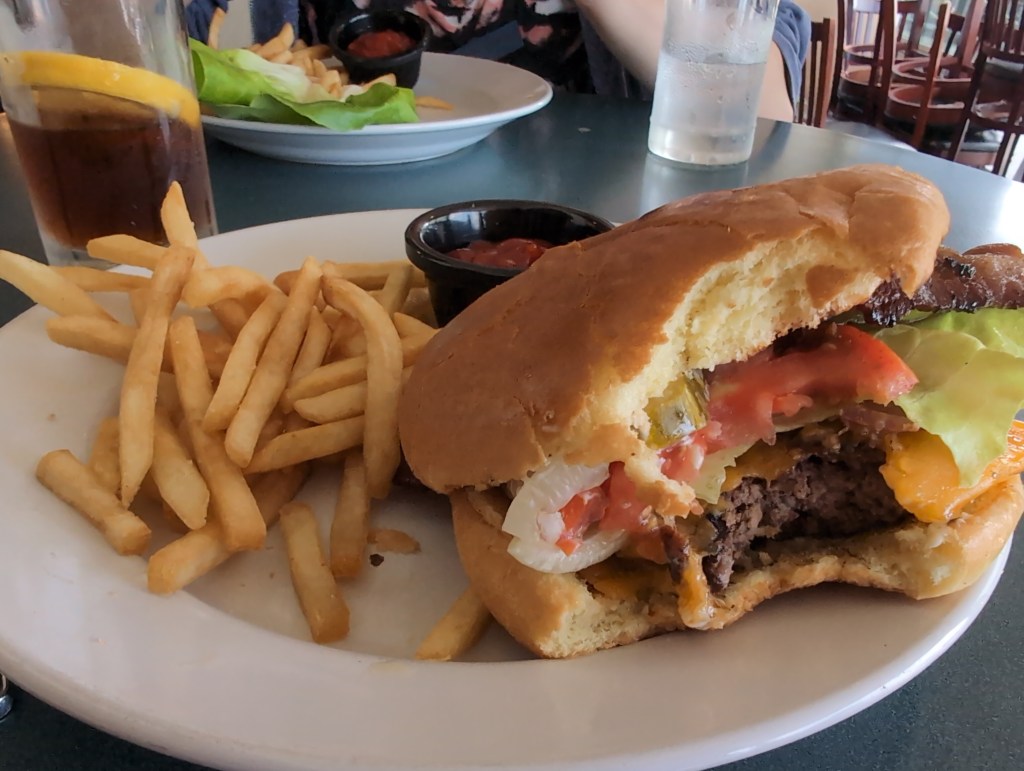 A partially eaten cheese burger sits on a plate with thin fries.