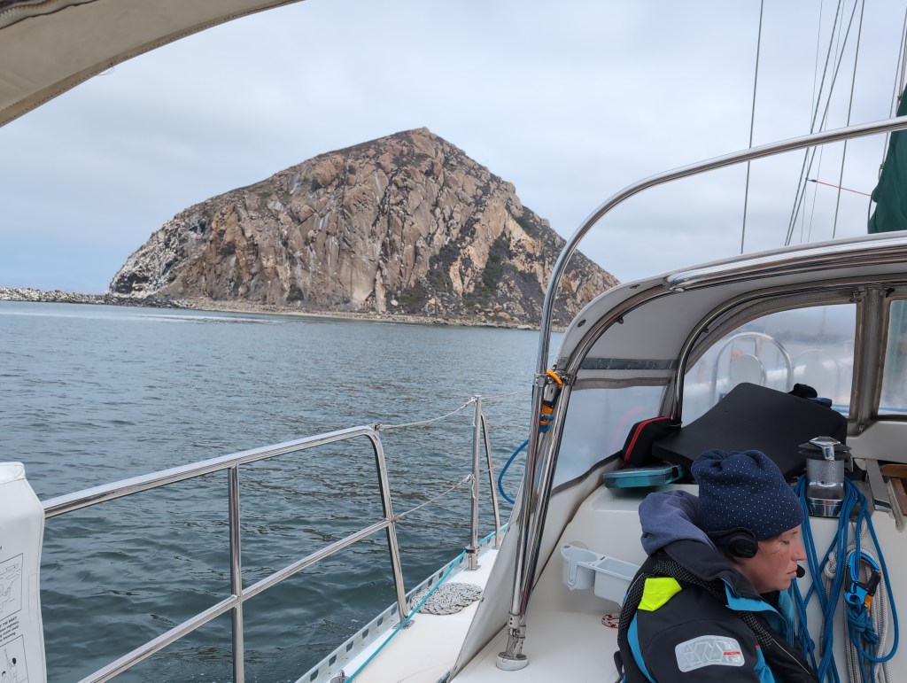 Tiffany sits in the cockpit as the boat passes a massive, dome shaped, rock formation.