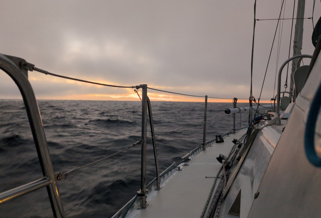 The sun rises across a choppy sea on an overcast morning.