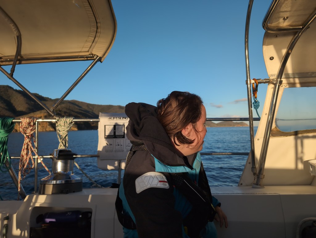 The morning light illuminated Tiffany as she looks out over the water from Luna Moth's cockpit. A hilly island lies over the water behind her.