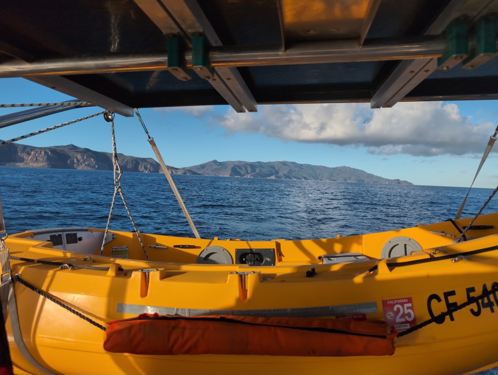 The view over Luna Moth's yellow plastic dinghy, hung off her stern, as she motors away from Santa Catalina Island.