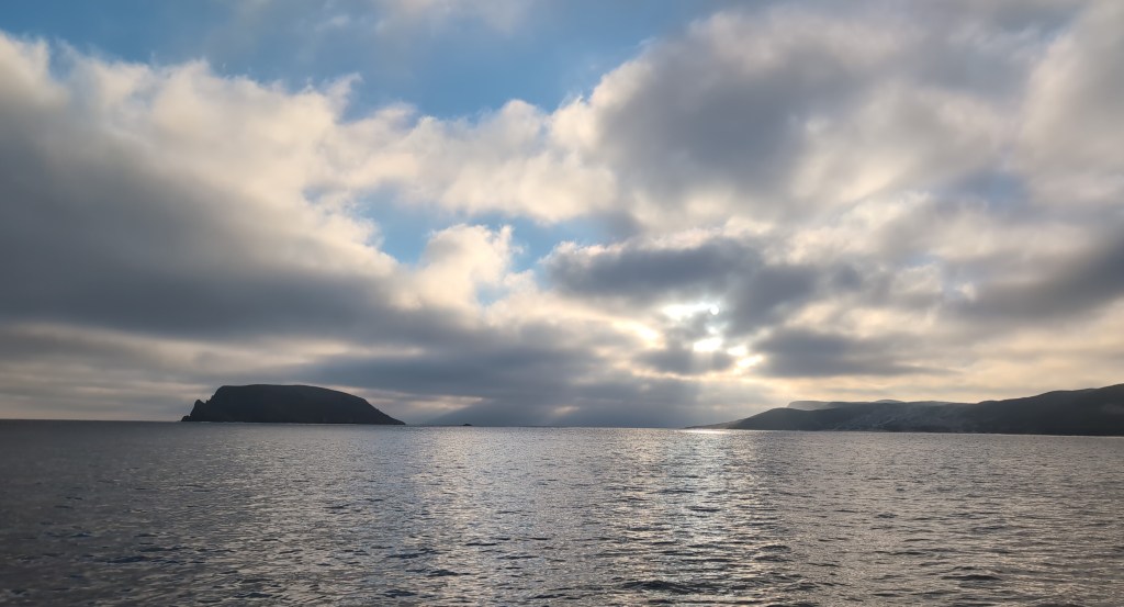 Dramatic clouds stretch to the horizon over a calm bay, a small island, and a point of land.