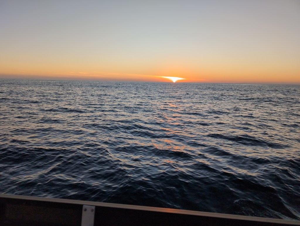 A calm sea stretches out to the horizon and a setting sun.