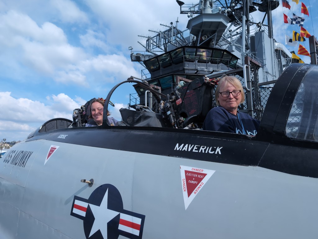 Tiffany and Lisa ham it up, sitting in the cockpit of a USS Midway flagged F-14 Tomcat. Beneath Lisa is the name "Maverick" and beneath Tiffany is "Goose".
