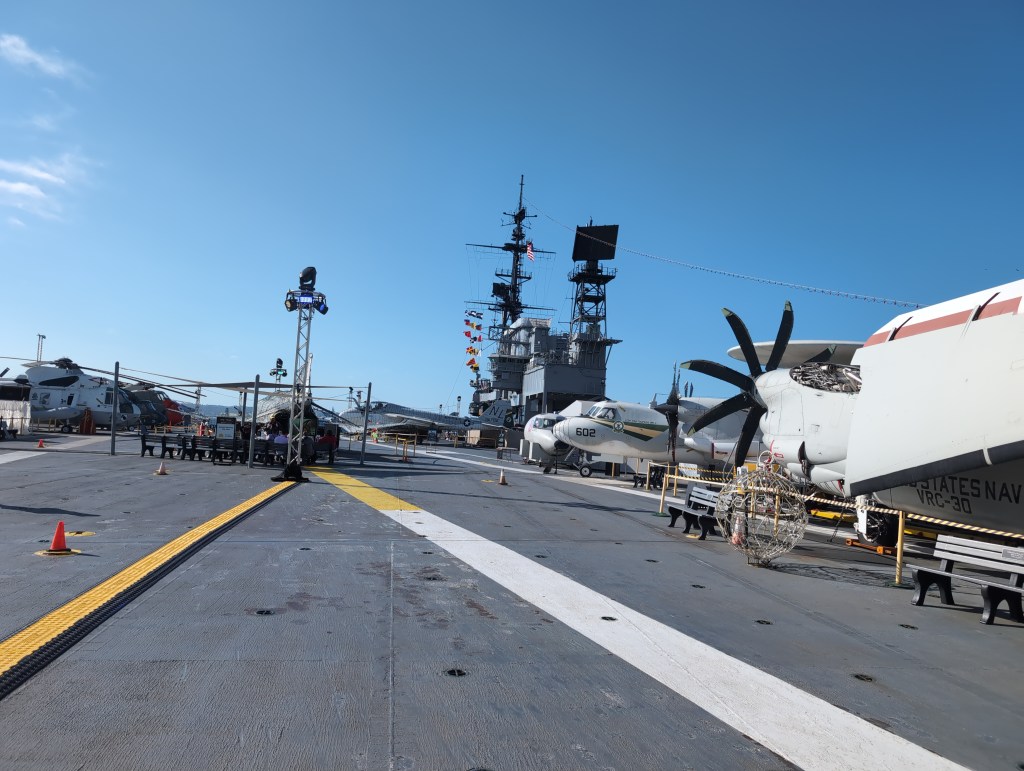 The flight deck of an aircraft carrier with numerous planes and helicopters on display.