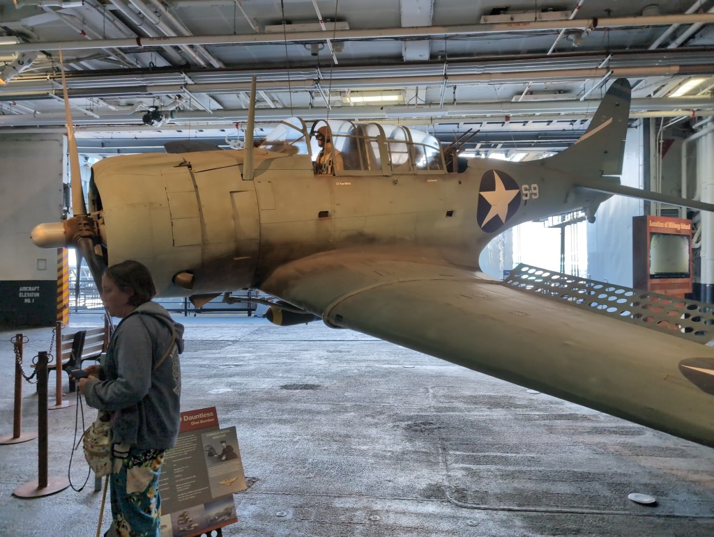 Tiffany, listening intently to her phone, stands before a small, World War II era, US fighter plane.