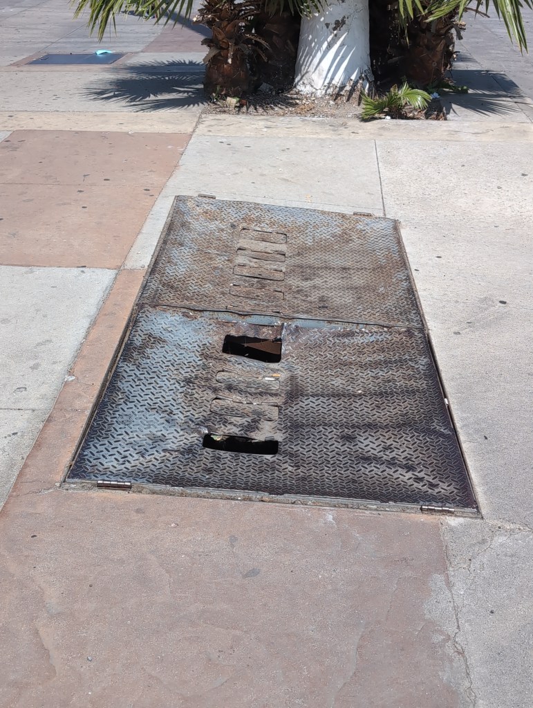 Two long metal hatches with open holes are dented in as if run over by a car.