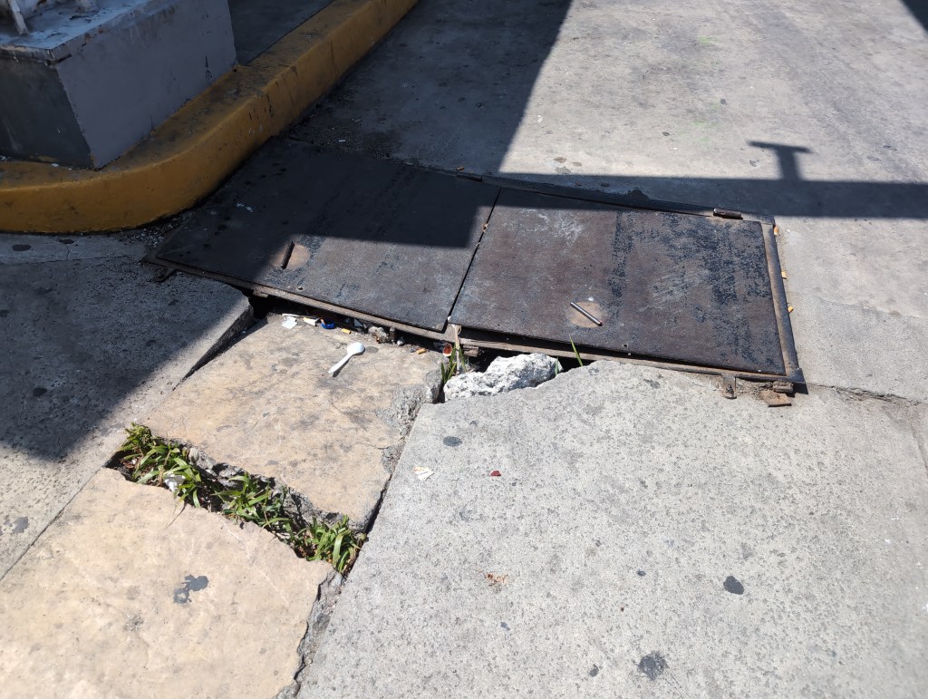 Colapsed sidewalk leads up a a metal hatch, one side of which is sticking up.