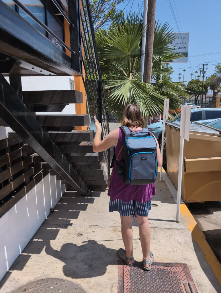 Tiffany walks down a narrow sidewalk, her hand up to avoid hitting a staircase that comes down in the walkway.